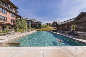 A swimming pool with clear water, surrounded by lounge chairs and a building with multiple floors.