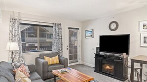 Una sala de estar con sofá, mesa de centro, chimenea, televisor y una ventana con cortinas.