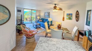 A spacious living area with a balcony, a dining table, and a ceiling fan. - Kauhale Makai #330 Oceanfront, Pool, Hot tub, A/C, Wi-Fi, Stunning Sunsets! (Kihei)