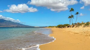 A beach with clear blue water, a sandy shore, and palm trees. - Kauhale Makai #330 Oceanfront, Pool, Hot tub, A/C, Wi-Fi, Stunning Sunsets! (Kihei)