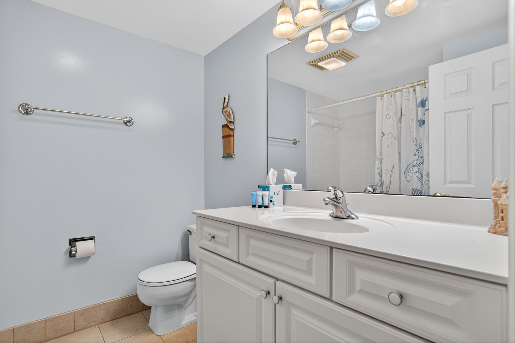 A bathroom with a white sink, a mirror, and a toilet. There are toiletries on the sink and a towel rack on the wall.
