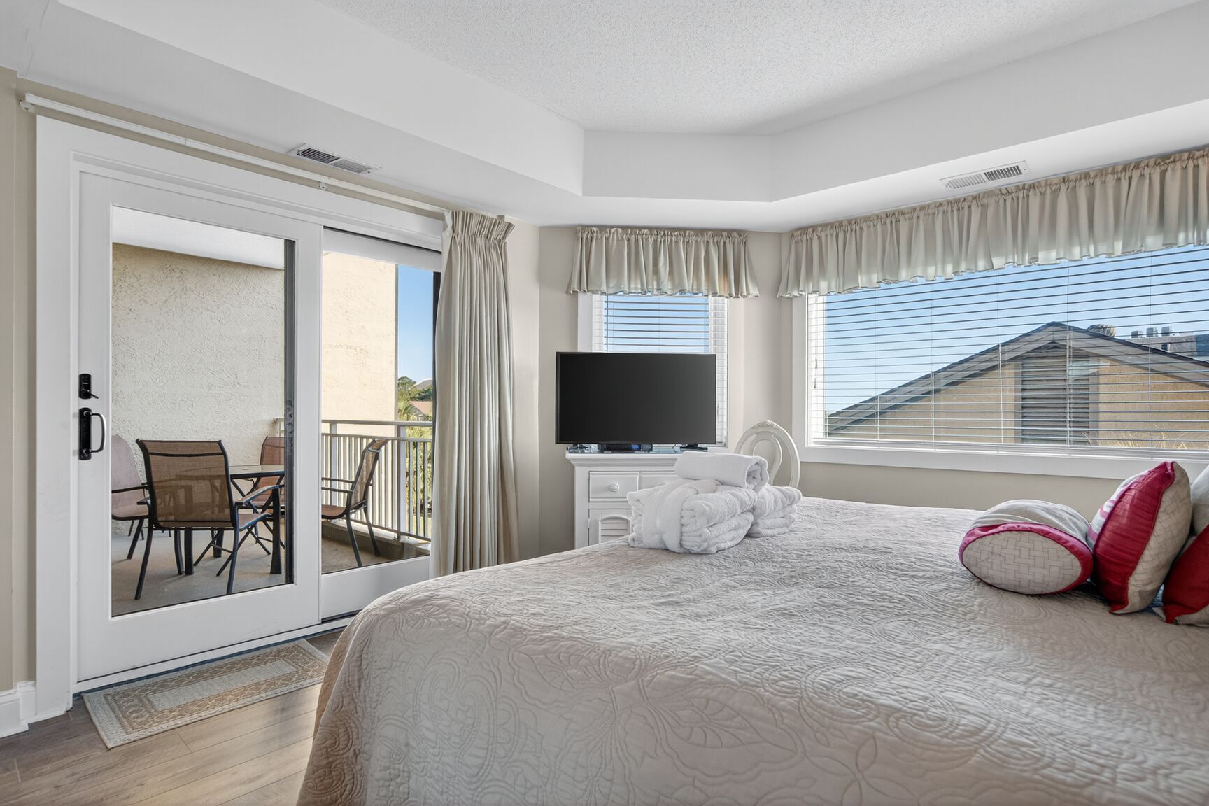 Ein Hotelzimmer mit einem großen Bett, einem Fernseher, einem Balkon mit Tisch und Stühlen sowie Blick ins Freie.