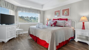 Ein Schlafzimmer mit Bett, Fernseher, Schreibtisch und Fenster mit Jalousien.