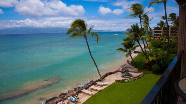 Ein Balkon mit Blick auf einen Strand, Palmen und einen klaren Himmel.