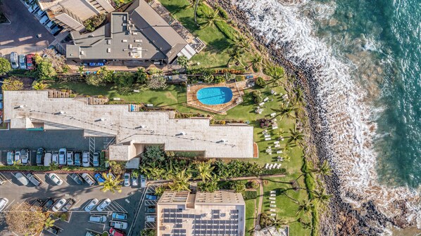 An aerial view of a coastal hotel with a swimming pool, parking area, and ocean view.