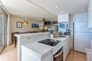 A modern kitchen with white cabinetry, a central island, a microwave, and a refrigerator. - Island Paradise Found: Comfort and Oceanfront Views at Kamaole Nalu #404 (Kihei)