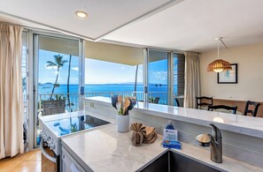 A modern kitchen with a large island, a dining area with chairs, and a view of the ocean.