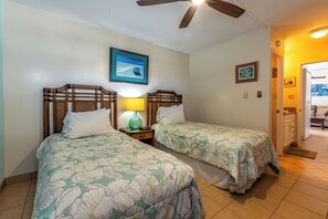 A room with two beds, a ceiling fan, a framed picture on the wall, and a door leading to another room.