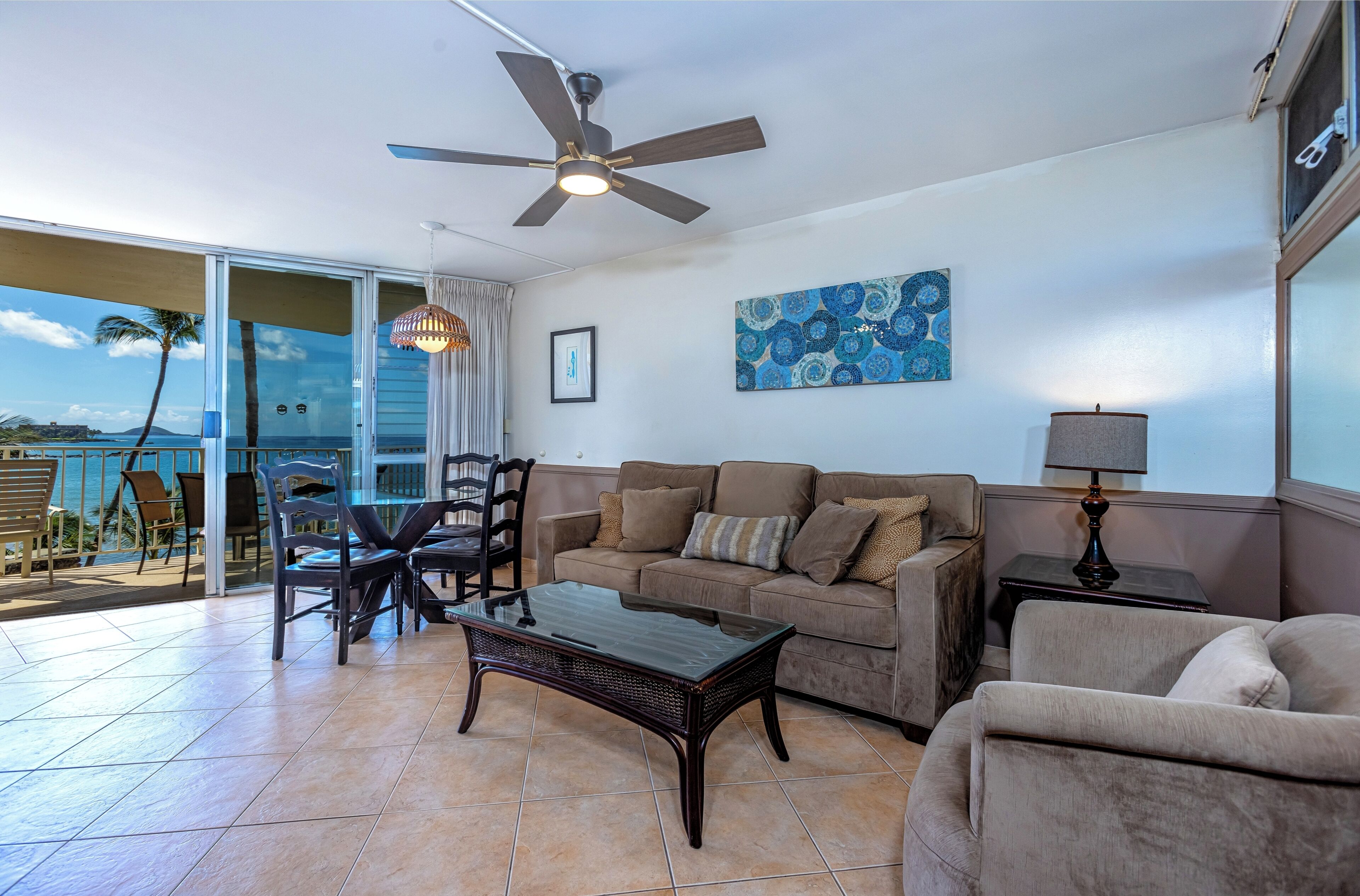 A living room with a glass door leading to a balcony, a ceiling fan, a sofa, a coffee table, and a lamp.
