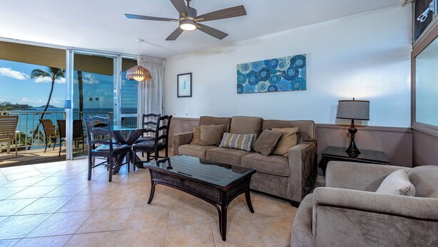 A living room with a glass door leading to a balcony, a ceiling fan, a sofa, a coffee table, and a lamp. - Island Paradise Found: Comfort and Oceanfront Views at Kamaole Nalu #404 (Kihei)