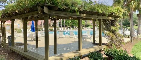A wooden pergola with a poolside area, including lounge chairs and a sign indicating a pool water temperature of 80°F.