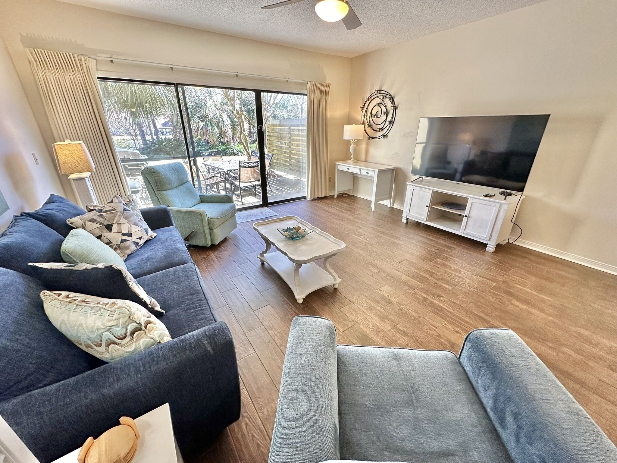 A living room with a large TV, a sofa set, a coffee table, and a view through the glass doors.