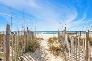 A sandy beach path leading to the ocean, surrounded by wooden fences and sparse vegetation.