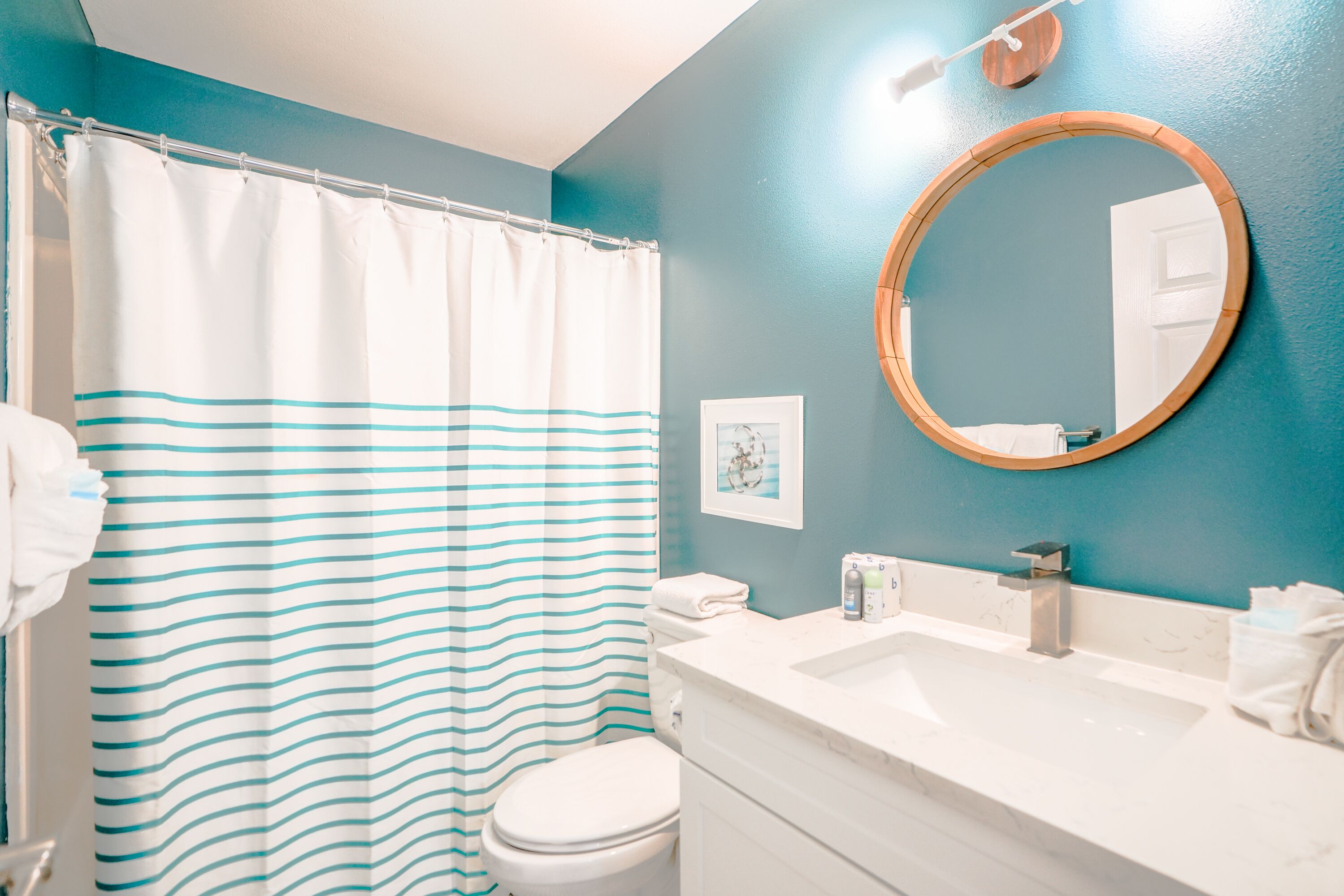 A bathroom with a striped shower curtain, a round mirror, a white sink, and a white toilet.