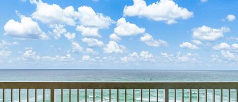 A beach view from a balcony with a railing, ocean waves, and scattered beach umbrellas.