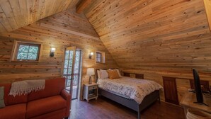 A cozy cabin bedroom with a sloped ceiling, wooden walls, a bed, a nightstand, a lamp, and a window. - Monarch Crest Chalet- Sauna and Pet Friendly (Salida)
