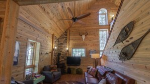 A cozy cabin interior with a stone fireplace, leather sofas, a television, and a ceiling fan. - Monarch Crest Chalet- Sauna and Pet Friendly (Salida)