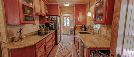 A narrow kitchen with wooden cabinets, granite countertops, and a patterned rug.