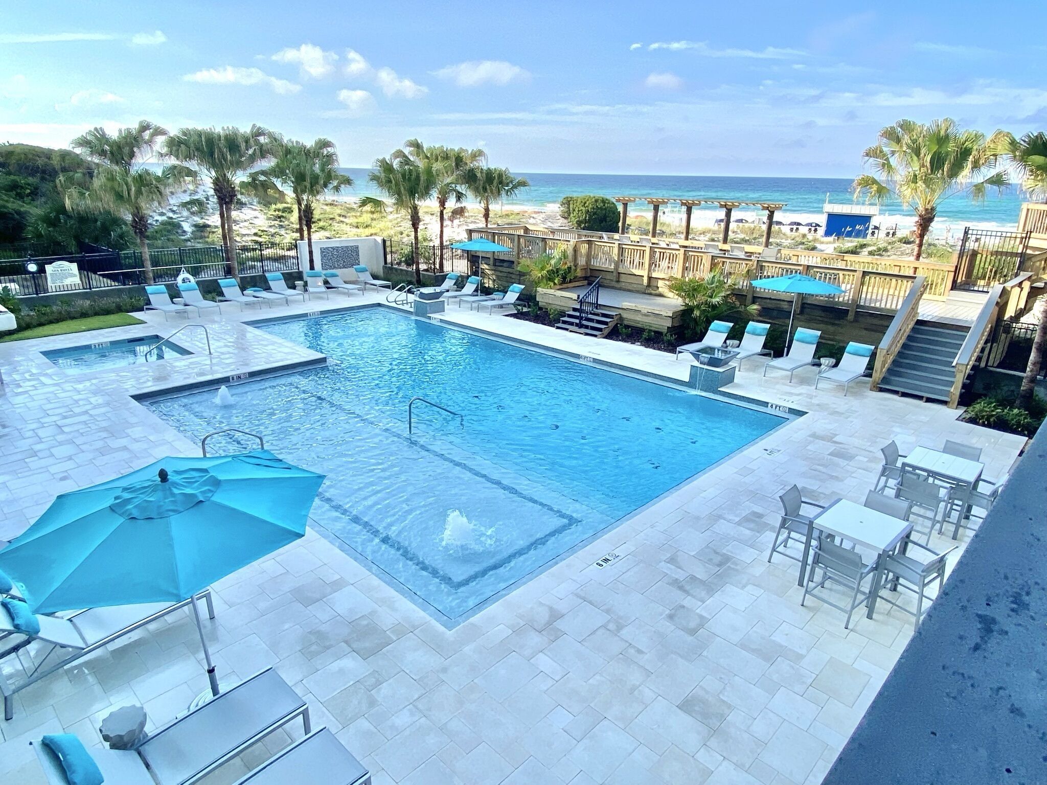 A pool area with lounge chairs, a small pool, and a view of the beach.