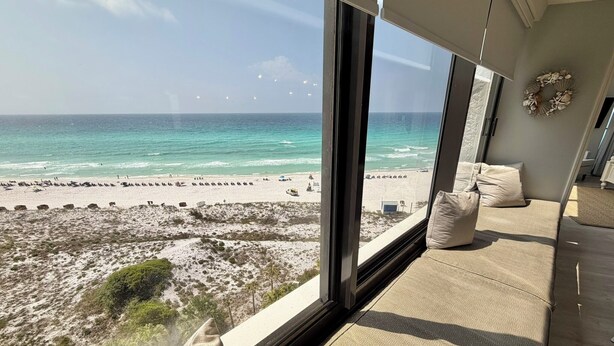 Una stanza con un'ampia finestra vista spiaggia, un letto con biancheria beige e una ghirlanda decorativa appesa al muro.