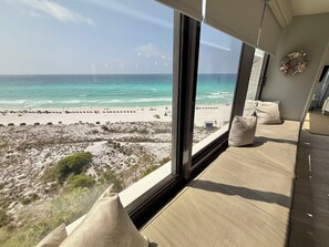 Une chambre dotée d’une grande fenêtre donnant sur une plage, d’un lit avec une literie de couleur beige et d’une couronne décorative accrochée au mur.