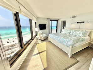 Une chambre avec une grande fenêtre, un lit, une chaise, un téléviseur et une vue sur la plage.
