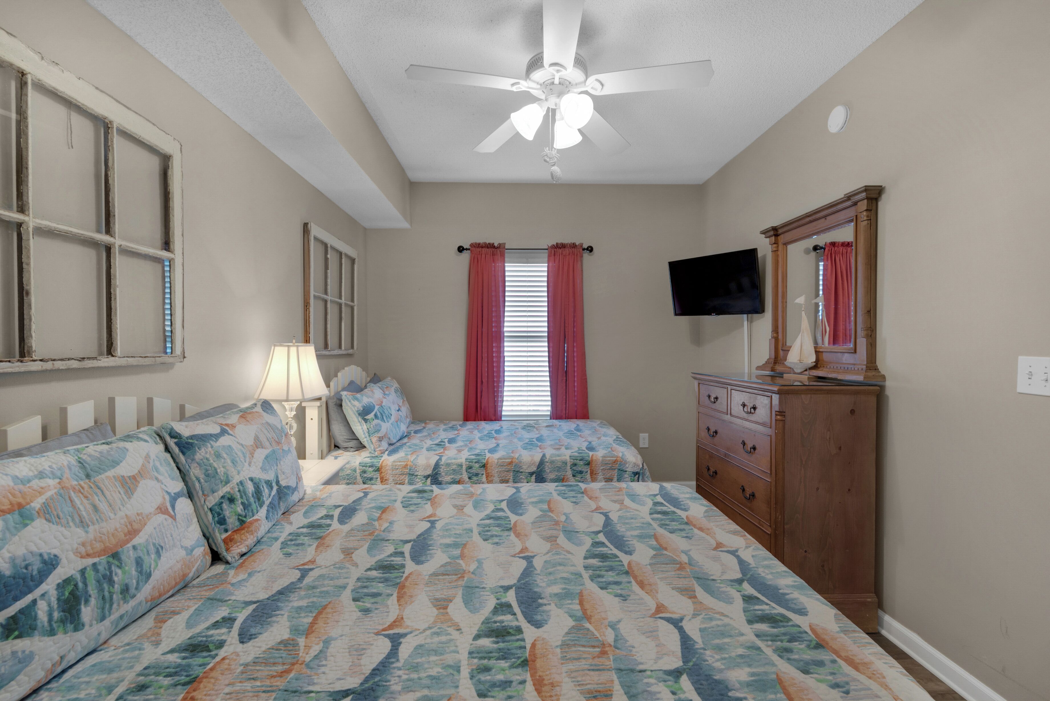 A bedroom with two beds, a ceiling fan, a dresser, a TV, and a window with curtains.
