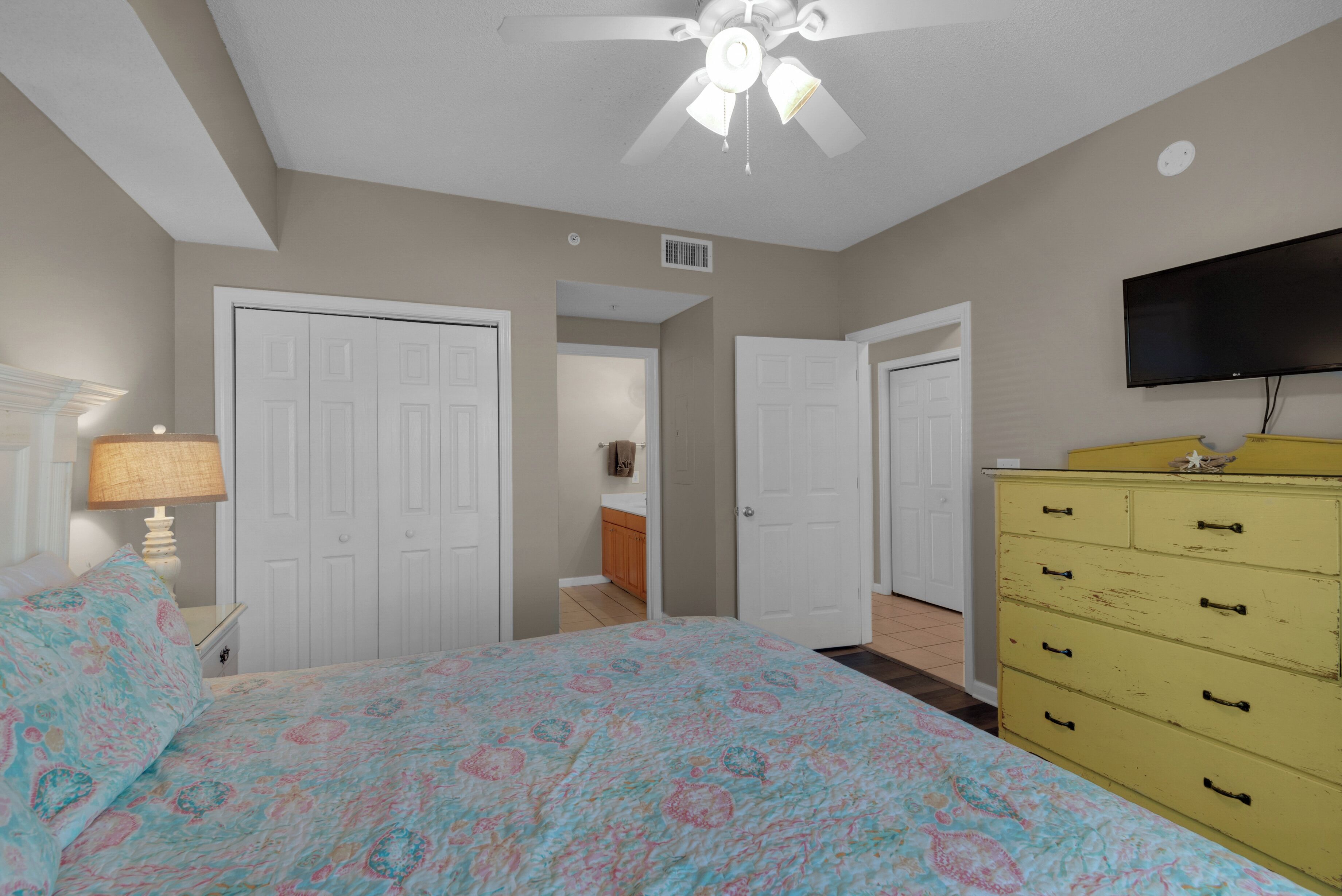 A bedroom with a bed, a ceiling fan, a television, and a dresser.