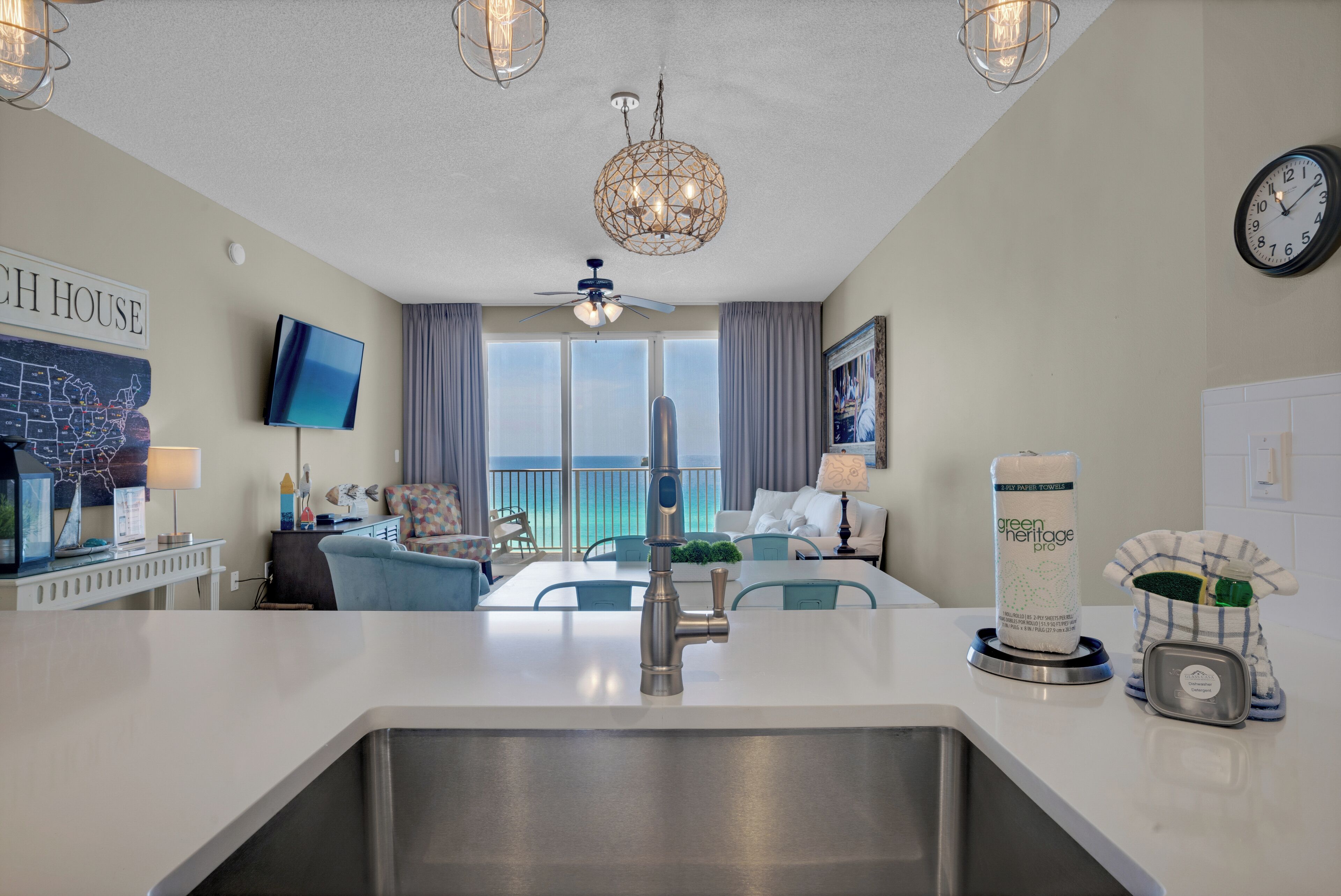 A modern kitchen with a stainless steel sink, a ceiling fan, and a large window overlooking the ocean.