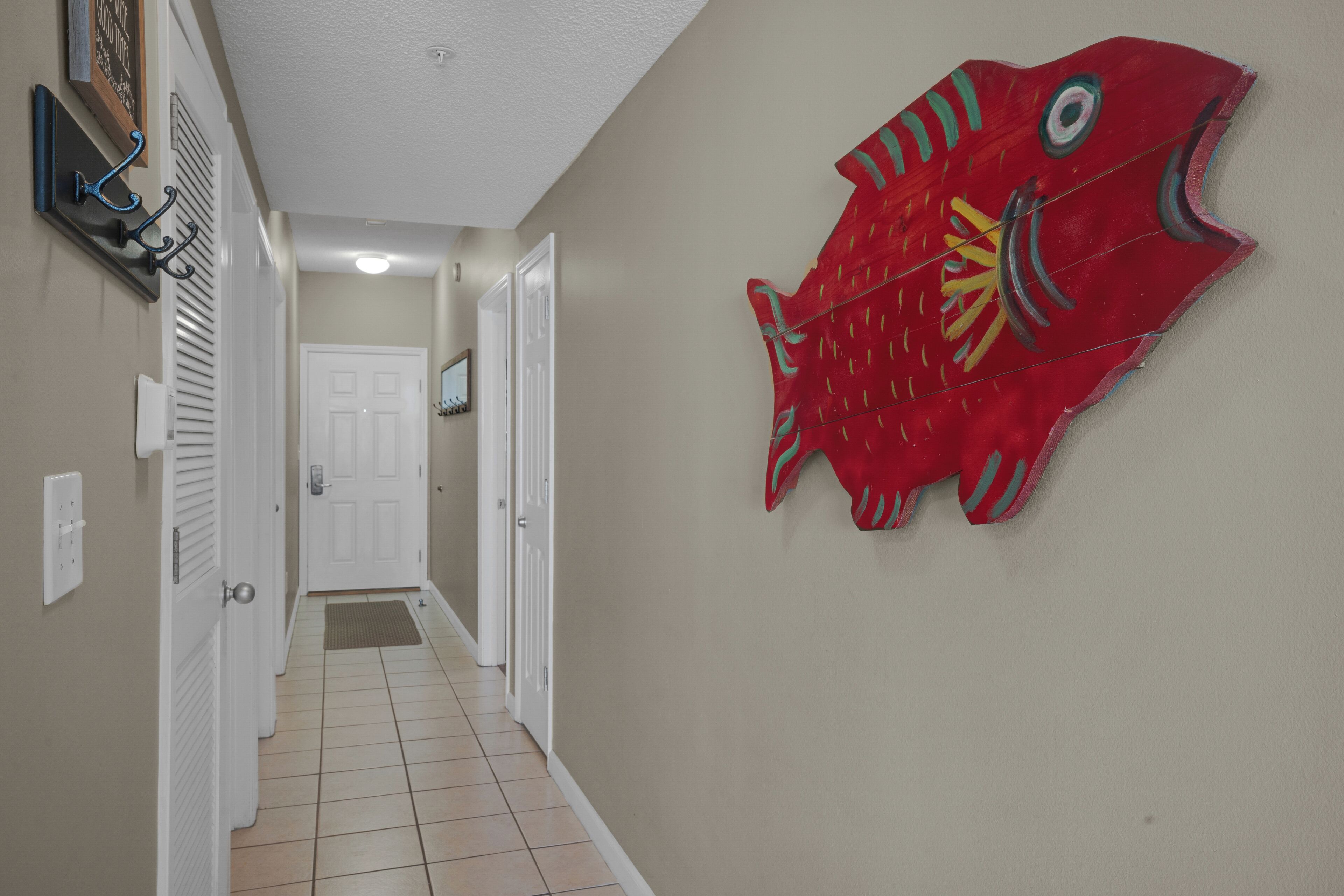 A hallway with a red fish decoration on the wall, white doors, and a tiled floor.
