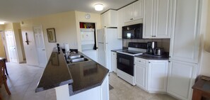 A kitchen with white cabinets, a black countertop, a stove, a microwave, and a sink.
