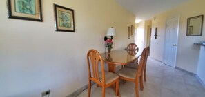 A dining area with a round table and four wooden chairs. There is a lamp on the table, and a potted plant with flowers.