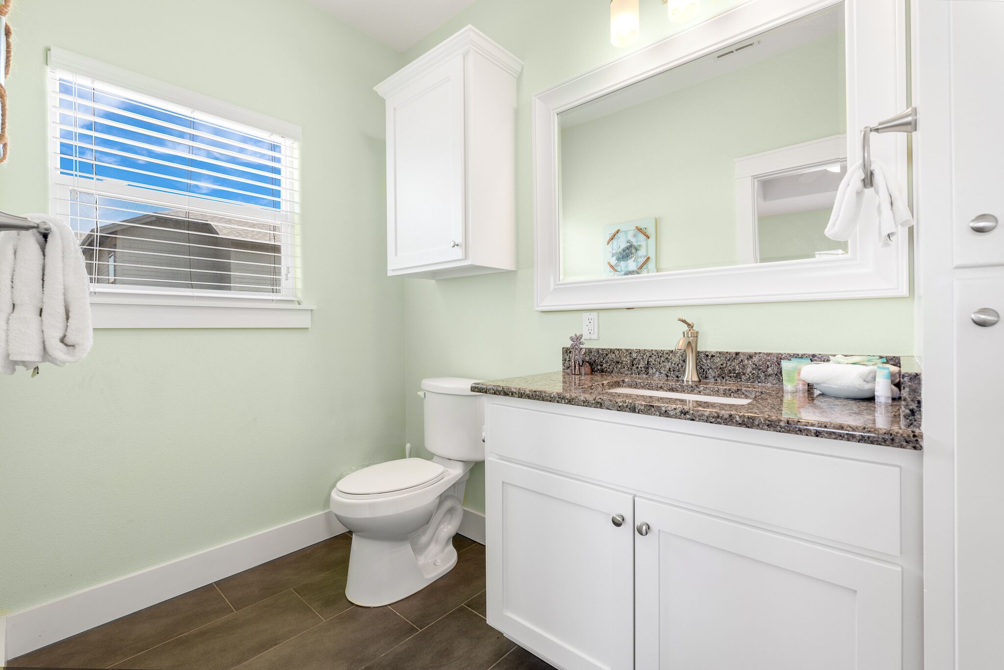 Une salle de bain comprenant des toilettes, un lavabo avec un plan de travail en granit et un miroir au-dessus du lavabo.