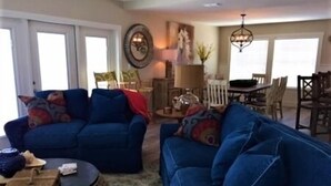 A living room with two blue sofas, a round coffee table, and a dining area in the background. - Three Bedroom, Three and a Half Bath. Private Boat Slip. Communal Pool. (Port Mansfield)