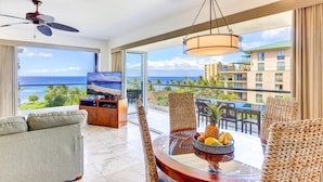 A spacious balcony with a view of the ocean, a television, wicker furniture, and a fruit bowl.