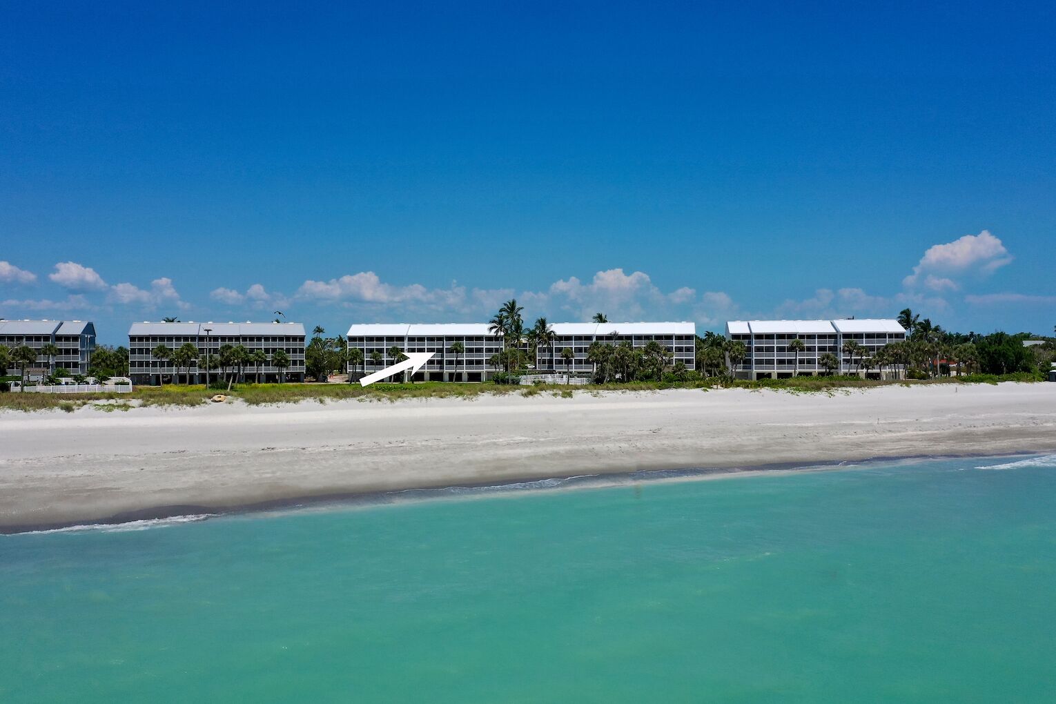 A beachfront hotel with multiple buildings, a sandy beach, and clear turquoise waters.