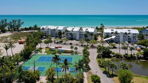Ein Resort mit mehreren weißen Gebäuden, einem Tennisplatz und Blick auf den Strand.