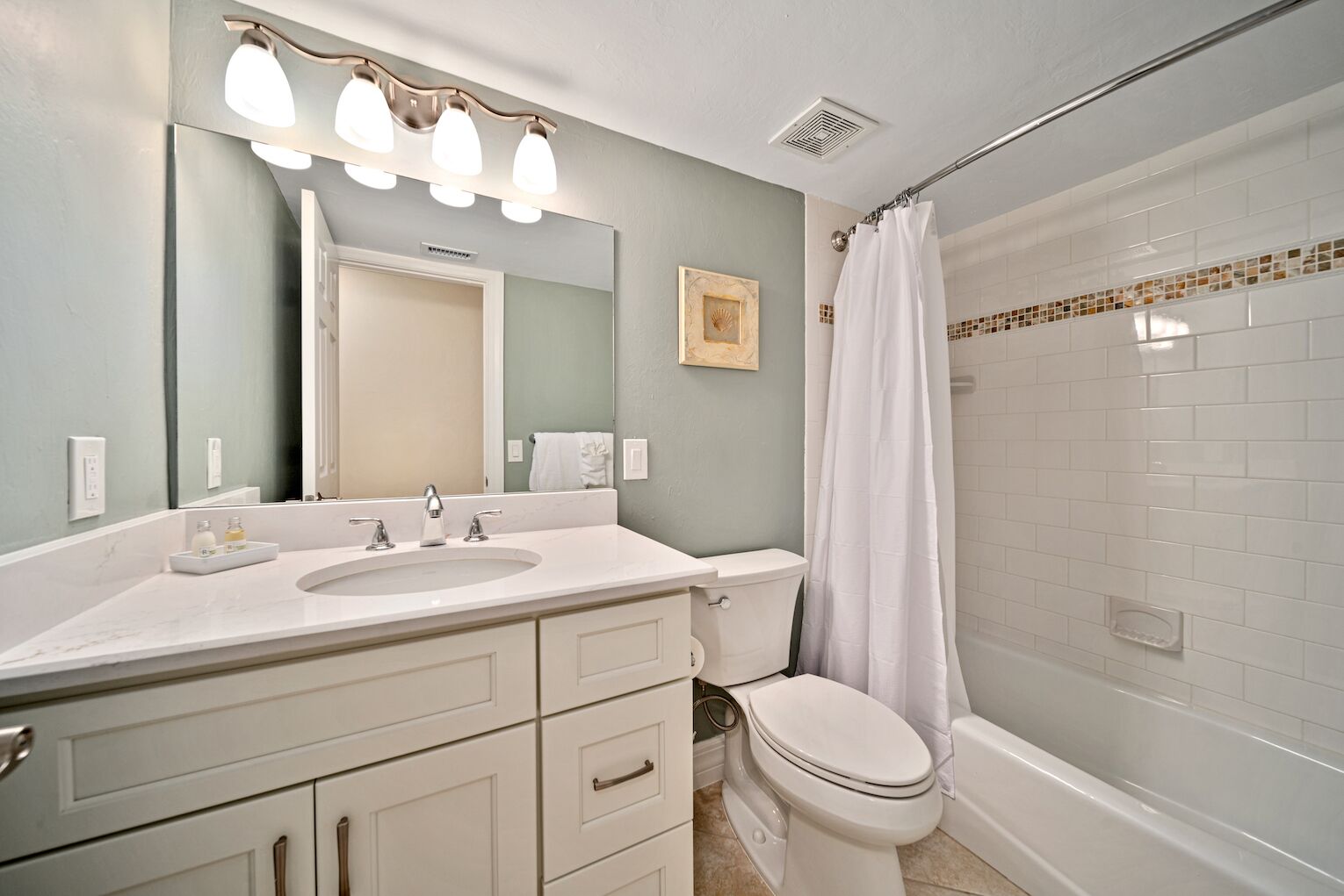 A bathroom with a white sink, mirror, and toilet. There is a shower curtain and a framed picture on the wall.