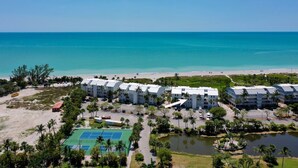 Ein Resort mit mehreren weißen Gebäuden, einem Tennisplatz und einem Strand.