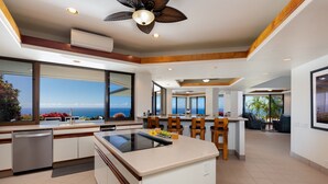 A modern kitchen with a central island, large windows offering ocean views, and a ceiling fan.