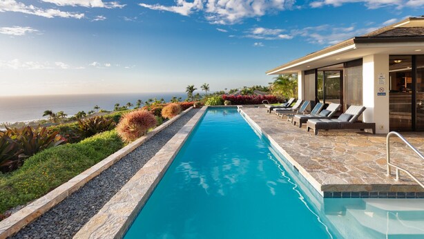 Una piscina con vista al océano, rodeada de plantas tropicales y sillones de descanso.