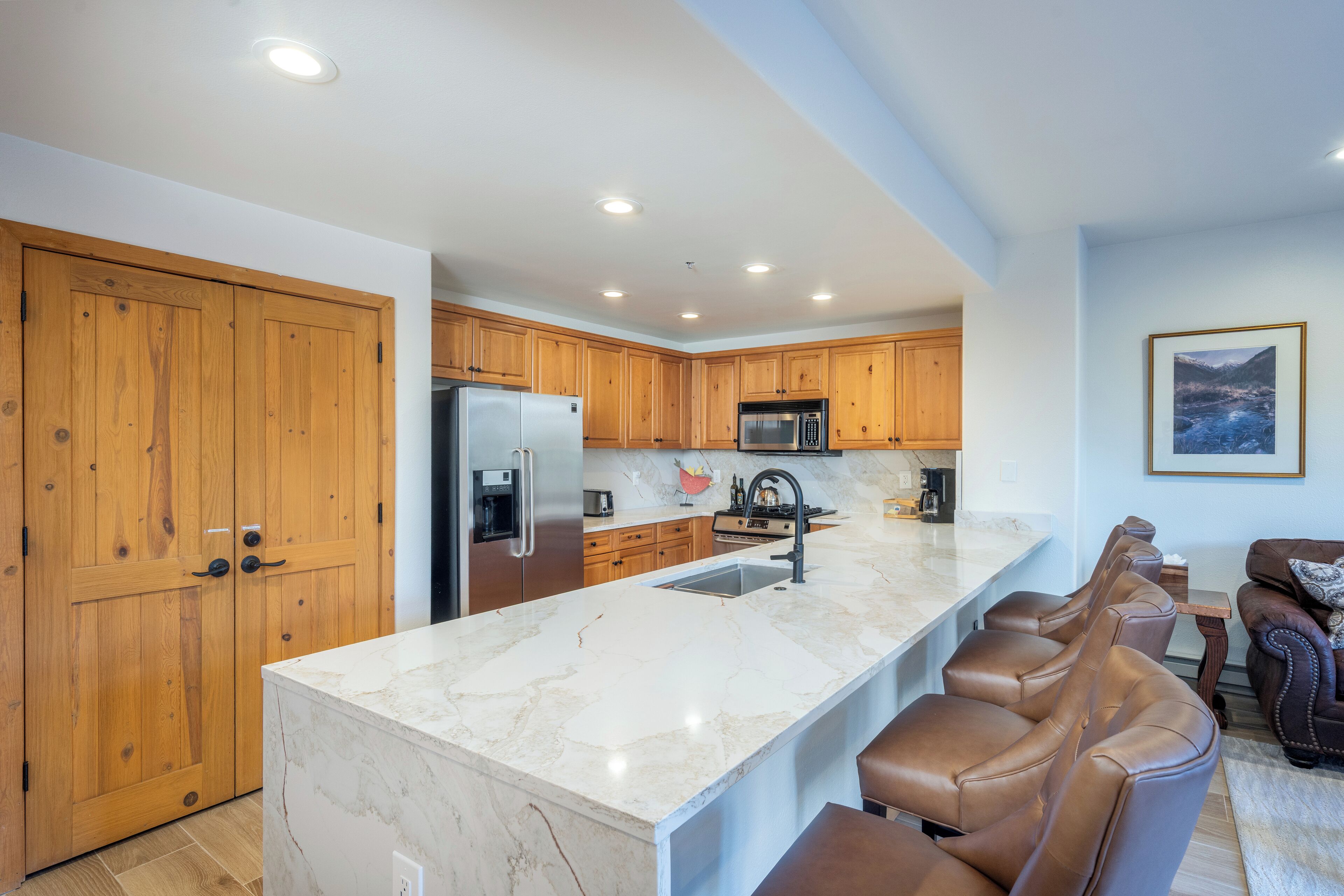 Una cocina moderna con armarios de madera, encimera de mármol y una barra integrada con taburetes de cuero.