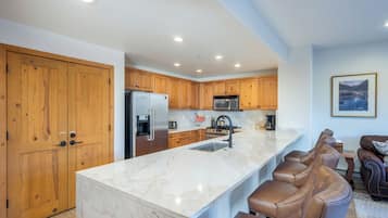 Una cocina moderna con armarios de madera, encimera de mármol y una barra integrada con taburetes de cuero.