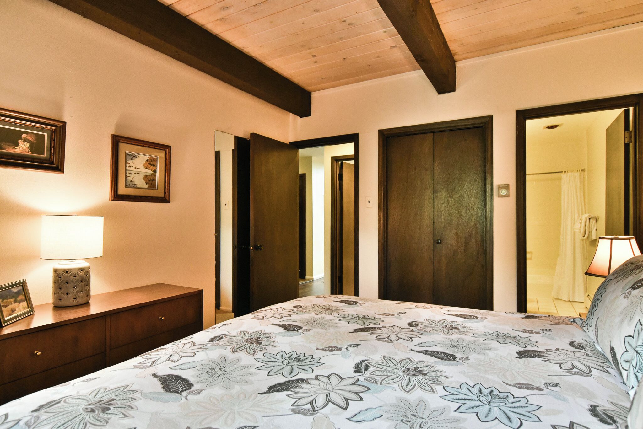 Ein Schlafzimmer mit einem Bett, einer Holzkommode, gerahmten Bildern und einer zur Toilette führenden Tür.