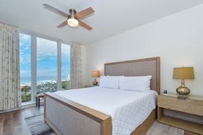 A hotel room with a large bed, two bedside tables, a ceiling fan, and a view of the beach. - Corner Condo w/ Gulf Views - Includes Beach Service -3BR St. Lucia 1001 (Destin)