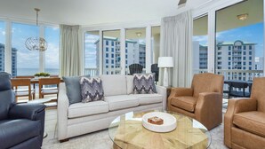Una sala de estar moderna con un sofá, sillones, una mesa de centro de vidrio y grandes ventanales con vistas a rascacielos.