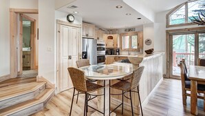 Een moderne keuken met houten kastjes, een roestvrijstalen koelkast en een glazen eettafel met rieten stoelen.