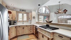 Een keuken met houten kastjes, een inbouwfornuis en een groot raam dat voor natuurlijk licht zorgt.