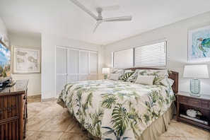 Un dormitorio con una cama, un ventilador de techo, una mesita de noche, una lámpara y un cuadro en la pared.