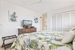 A bedroom with a bed, a TV on a wooden cabinet, a ceiling fan, and a wardrobe with louvered doors.